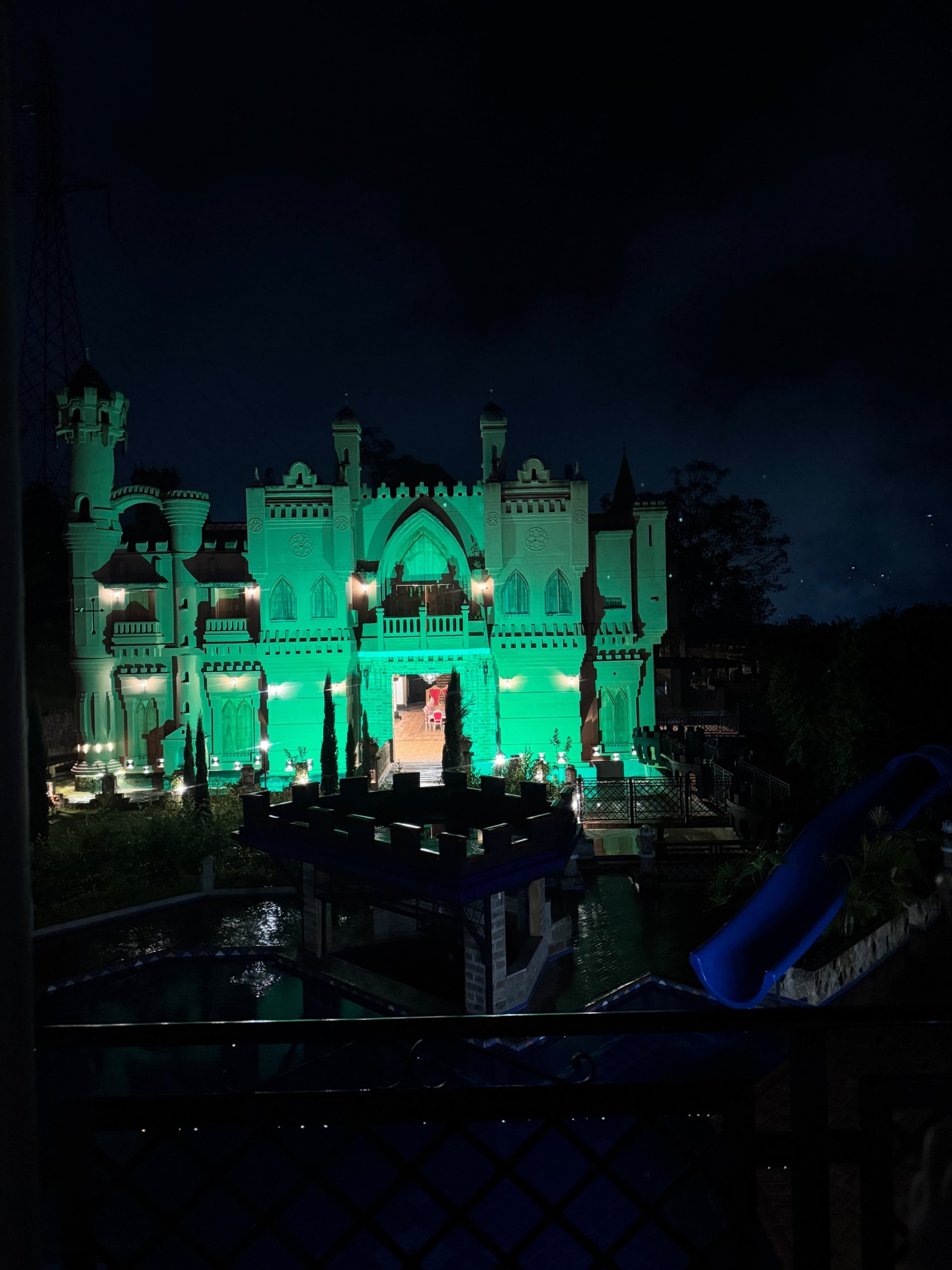 The castle illuminated in green at night with the pool and water slide below
